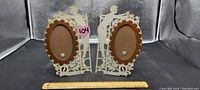 Front view of the two handcrafted celluloid picture frames, showing intricate silhouette designs and oval photo holders with scalloped edges and heart details.