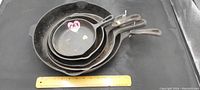 Top view of stacked five cast iron frying pans showing size variation and long handles.
