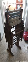Full view of the foldable wooden clothes wringer washer standing upright on a tiled floor in a narrow hallway, showing structural details and folding mechanism.