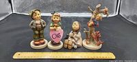 Photo showing all four German Hummel porcelain figurines laid out in front of a ruler for size reference.