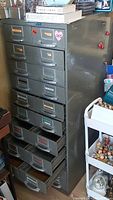 Front angle of tall grey steel card file cabinet showing multiple drawers with label holders