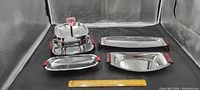 Overall view of six chrome serving dishes of various sizes with red handles arranged with a ruler for scale