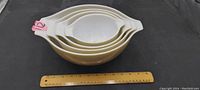 Stacked photo of four Pyrex mixing bowls showing white interiors and golden butterfly design exterior with a ruler for scale.