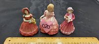 Three Royal Doulton porcelain figurines about 5 inches tall shown together on a black surface with a ruler for scale.