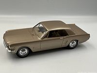 Side angle of metallic beige 1966 Ford Mustang toy car showing full body and wheels.