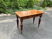 Three-quarter view showing the tabletop, front apron with two drawers and turned, fluted legs