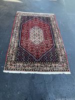 Full view of red and navy oriental rug with ivory border and fringe on asphalt surface