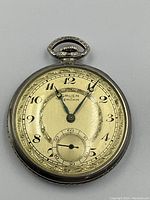 Front view of pocket watch face showing dial, hands, branding and sub-seconds.