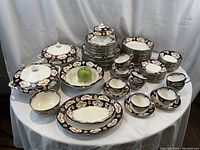 Full spread of all 87 pieces on round table with white tablecloth and green apple reference