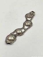 Single silver bracelet displayed flat to show length and design of four dome-shaped elements linked by double curb chain.