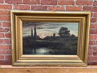 Full front view of framed oil landscape painting against brick wall