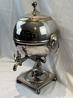 Front angle view showing entire urn: spigot, figural support, ring handles and hinged lid with finial