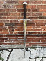 Full view of sword without sheath leaning against brick wall