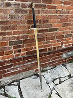 Full-length view of sword standing against brick wall showing overall shape and length