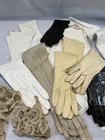 Grouping of assorted vintage gloves including white, beige, black leather gloves and tan lace gloves laid out on gray background.
