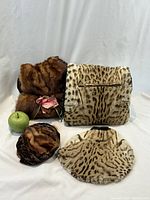 Full lot view with two muffs/purses at back, two hats at front, green apple for scale