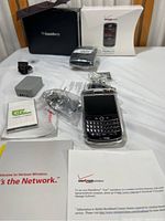 Blackberry Tour cell phone with all accessories including battery, charger, cables, protective case, original box, and Verizon pamphlets on a white surface.