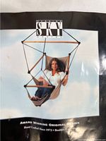 Photo of branded packaging showing a seated woman demonstrating the hanging Sky Chair. Includes brand logo and product design details.