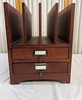 Front view of hardwood magazine rack showing five vertical dividers and two drawers with metal label holders.