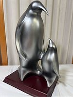 Front view of the Herco composite penguin statuette showing two silver penguins on a dark wooden base.