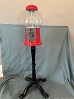 Full view of the vintage red gumball machine on black cast iron stand, showing overall condition and height.