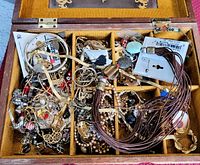 Top view of wooden box with multiple compartments containing assorted vintage costume jewellery pieces in a jumbled arrangement.