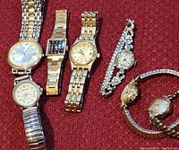Full overview of 7 vintage wristwatches showing variety of case shapes and band styles on a red textured fabric background