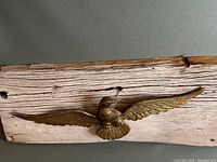 Close-up view of brass eagle mounted on rustic wooden board showing detailed feathers and wood texture