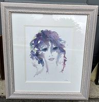 Framed Seriolithograph artwork showing a woman's portrait in purple tones, depicting the entire framed piece in a beige decorative frame.
