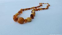 Close-up image of an amber bead necklace laid on a blue surface, showing a variety of amber beads with different shapes and colors ranging from light honey to darker brownish tones.