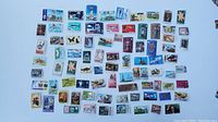 Wide view of about 60 assorted postage stamps showing various images on white background including animals, people, flowers, and historic subjects.