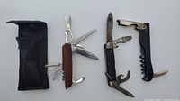 Three multi-tools and a corkscrew/bottle opener arranged with a black nylon case visible
