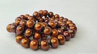 Close-up photo of glossy brown pearls arranged in a coil, showing color and surface texture.