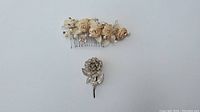 Hair comb with champagne colored roses and sparkling beads next to rose-shaped filigree brooch on white background.