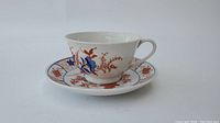 Side view of the Japanese porcelain cup and saucer, detailing floral and geometric decorations in red, blue, and rust color tones.