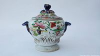Full view of the porcelain sauce tureen with floral-patterned body, blue handles, and blue finial on lid