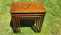 Top view of four stacked teak nesting tables showing wood grain and scratches on tabletop