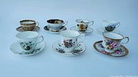 Seven teacups and matching saucers arranged and photographed together on a flat surface showing each piece's pattern and style.