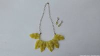 Full view of necklace with carved yellow stone leaves and pair of matching yellow dangle earrings on a light background.