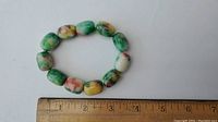 Top view of multicolor oval stone bead bracelet placed next to a ruler showing bead size around 1.5 cm each.