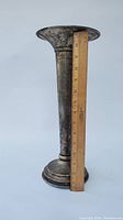 Side view of the tall metal trumpet vase alongside a wooden ruler showing it is about 15.5 inches tall.