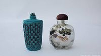 Front view of two Chinese snuff bottles: blue carved bottle and painted glass bottle with brown top.