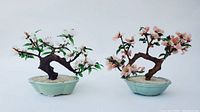 Pair of jade tree figurines with white and pink flowers in celadon pots on a white background.