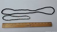 Overhead photo showing the full length of both necklaces alongside a ruler for scale; displays small uniform black beads and irregular turquoise and coral stones