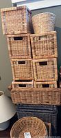 Stacked baskets including rectangular and square woven baskets on dark floor next to lamp.