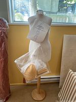 Front view of the Fabulous Fit dress form showing the torso shape on wooden stand with a bag of accessories attached.