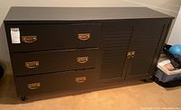 Front view of the black painted wooden dresser with three drawers on the left and shutter style cabinet doors on the right.