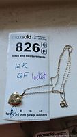 Photo of the gold filled heart-shaped locket on a fine chain with inventory tag showing "12K GF locket" handwritten.