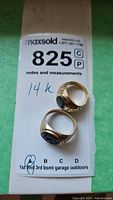 Two gold rings on MaxSold lot sheet: one larger carved intaglio ring, one smaller plain onyx ring