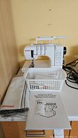 Front view of the Janome CoverPro 1000CPX serger on table with carrying handle, dust cover, instruction manual, basket and cords